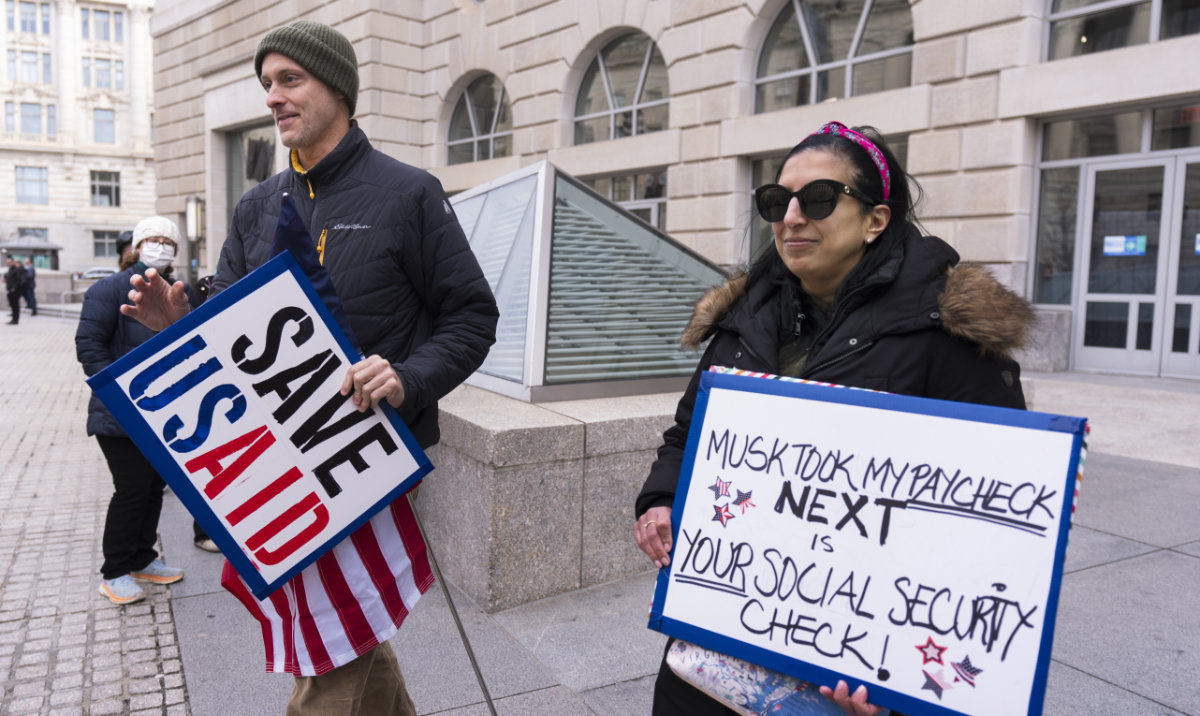 United States Agency for International Development, or USAID contract worker Priya Kathpal, right, and Taylor Williamson, left, who works for a company doing contract work for USAID, carry signs outside the USAID headquarters in Washington, Monday, Feb. 10, 2025. (AP)