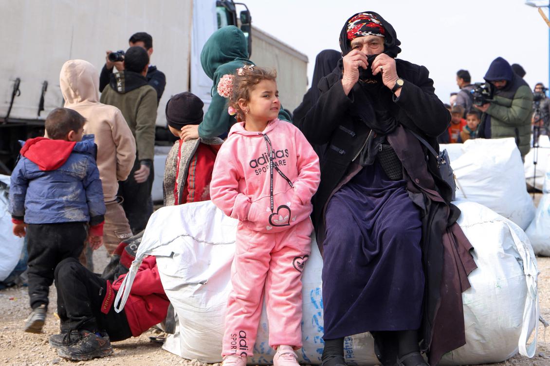 An elderly woman sits with a child by their belongings as they prepare to depart from the Al-Hol camp on Feb. 9, 2025, bound for Iraq in a coordinated departure between the Iraqi government and anti-Daesh coalition forces. (AFP)