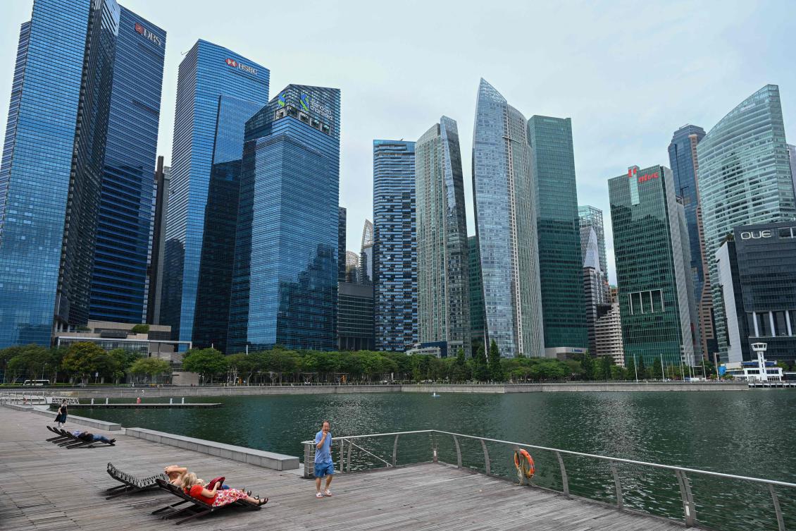 People rest on a bench along the boardwalk at Marina Bay next to the city skyline in Singapore on February 18, 2025. (AFP)
