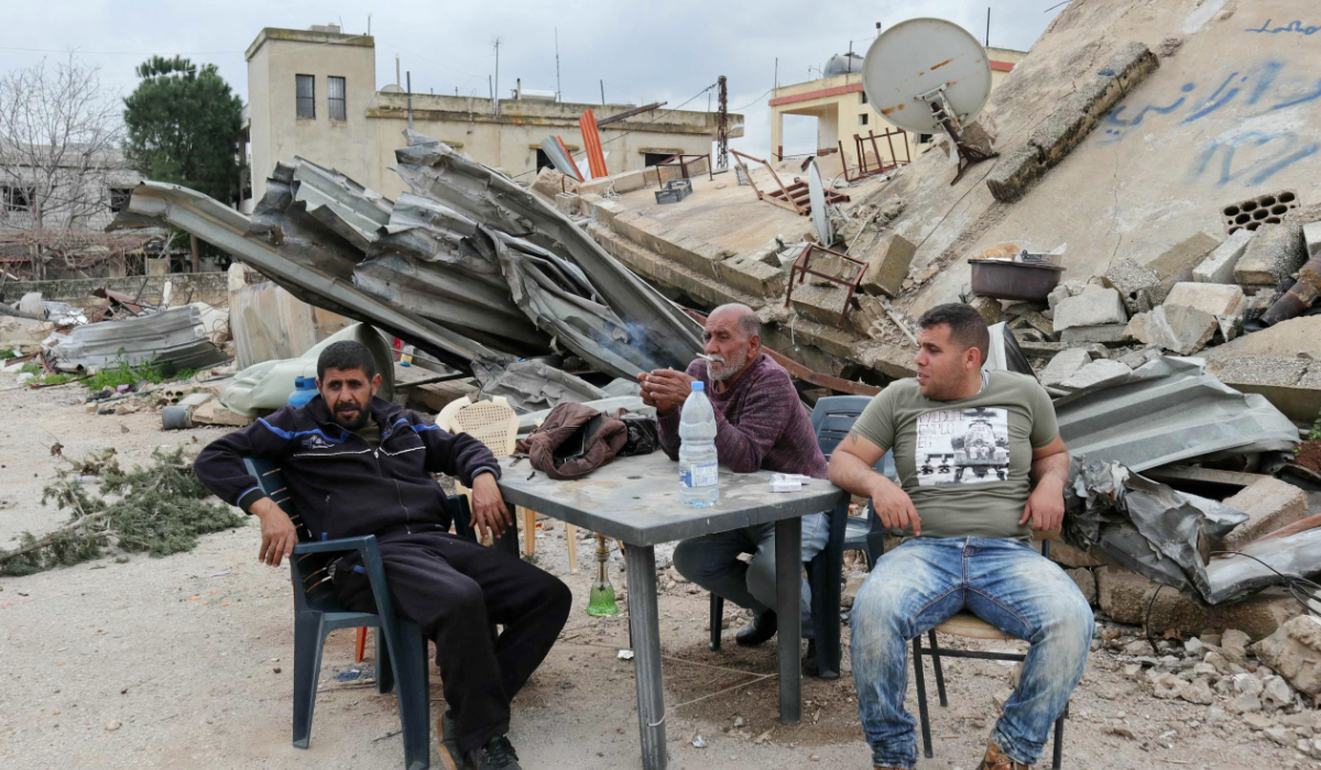 Men sit around a table in front of their destroyed house in the southern Lebanese border village of Wazzani after Israeli forces pulled out, on February 19, 2025. (AFP)