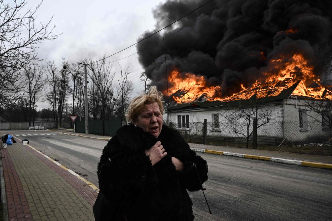 A woman stands in front of a house burning after being shelled in the city of Irpin, outside Kyiv. More than 1.2 million people have fled Ukraine into neighboring countries since Russia launched its full-scale invasion. (AFP)