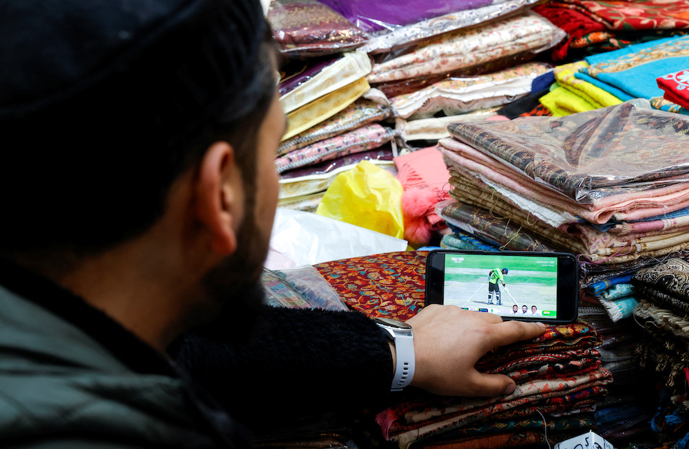 A Kashmiri shopkeeper watches the ICC Men’s Champions Trophy match between India and Pakistan on a mobile phone in Srinagar on Feb. 23, 2025. (Reuters)