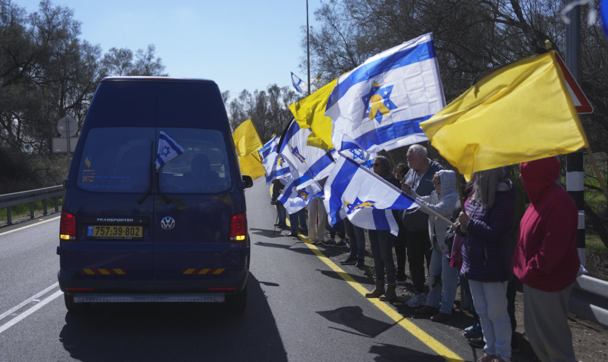 Mourners wave Israeli flags as the car carrying the coffin of former Israeli hostage Oded Lifshitz passes by at the entrance of Kibbutz Nir Oz, where his funeral will take place, in southern Israel, on Tuesday, Feb. 25, 2025. (AP)