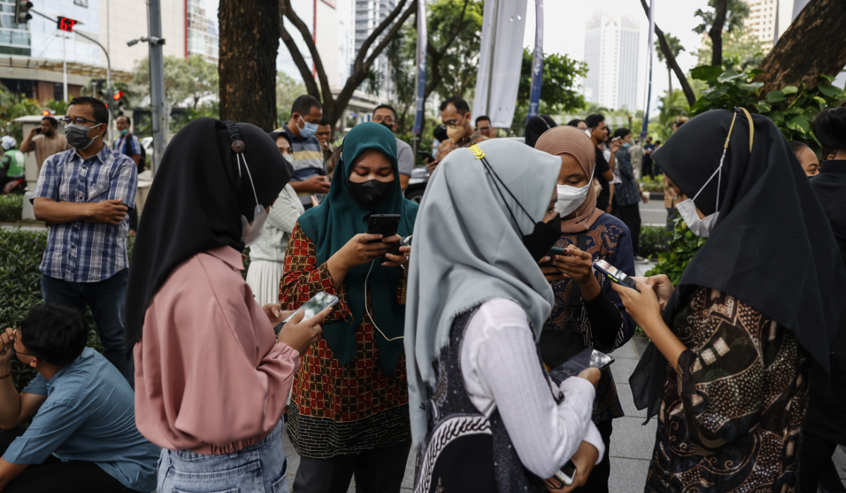 Office employees check their phones as they wait outside of an office tower amid fears of aftershocks following an earthquake at a business district in Jakarta, Indonesia, 14 January 2022. (EPA)