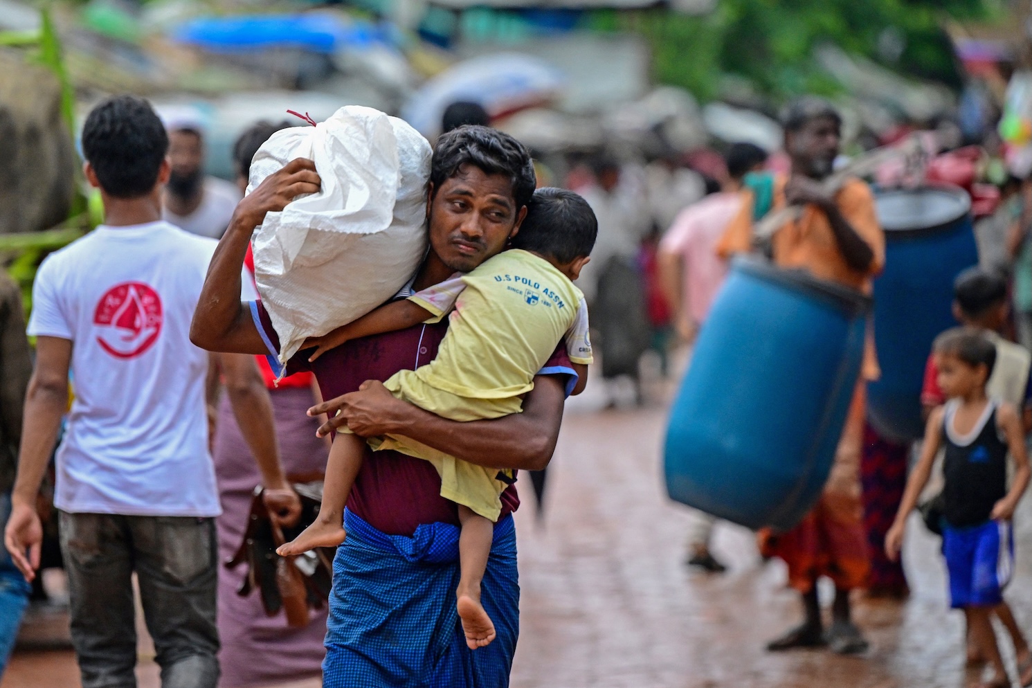 In this photo taken on Sept. 12, 2024, a Rohingya refugee man holds his child while carrying relief material at a camp in Ukhia, Bangladesh. (AFP)