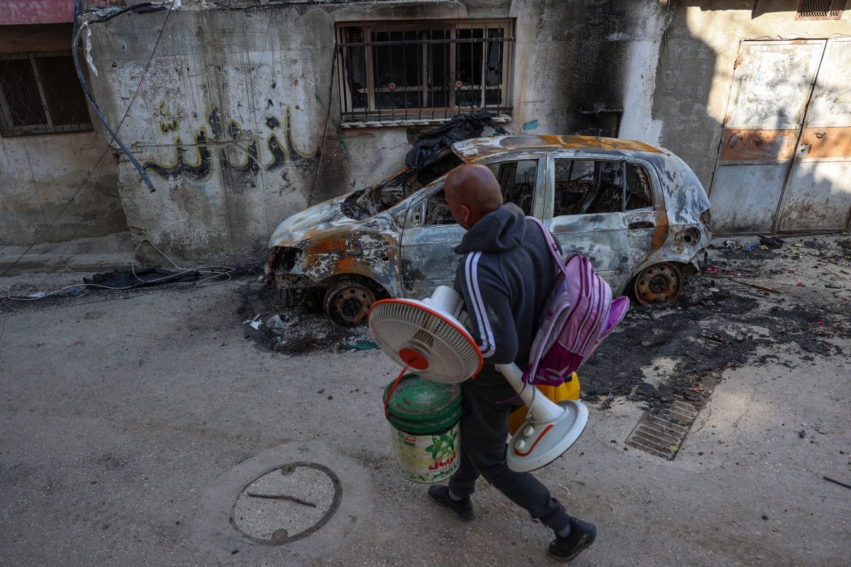 A man carries housewares as he walks past a burnt car while fleeing the Nur Shams camp for Palestinian refugees near Tulkarem (AFP)