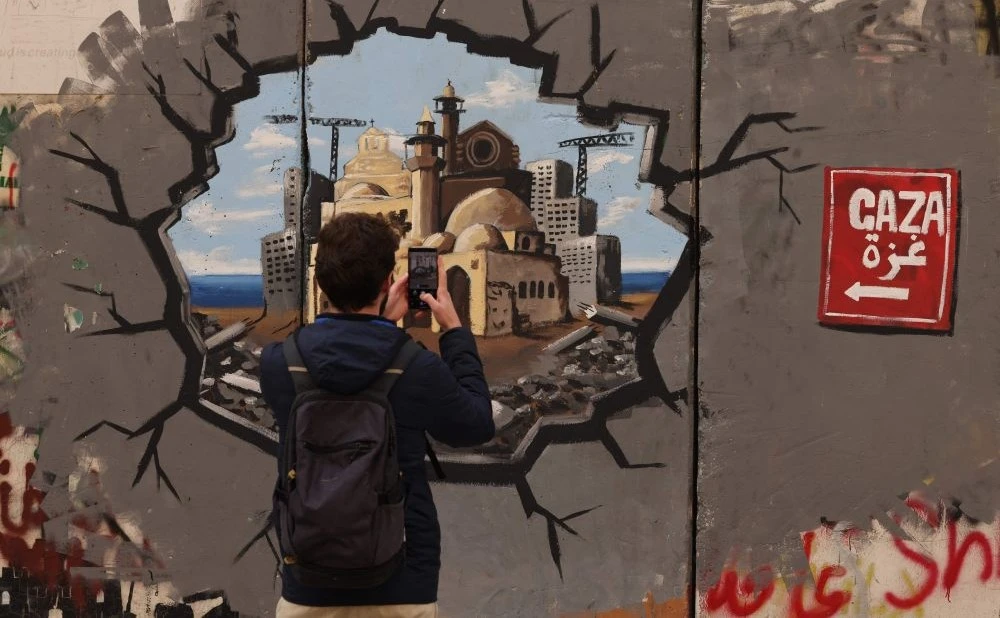 A man takes a picture of graffiti representing the reconstruction of Gaza, Bethlehem, occupied West Bank, Feb. 12, 2025. (AFP)