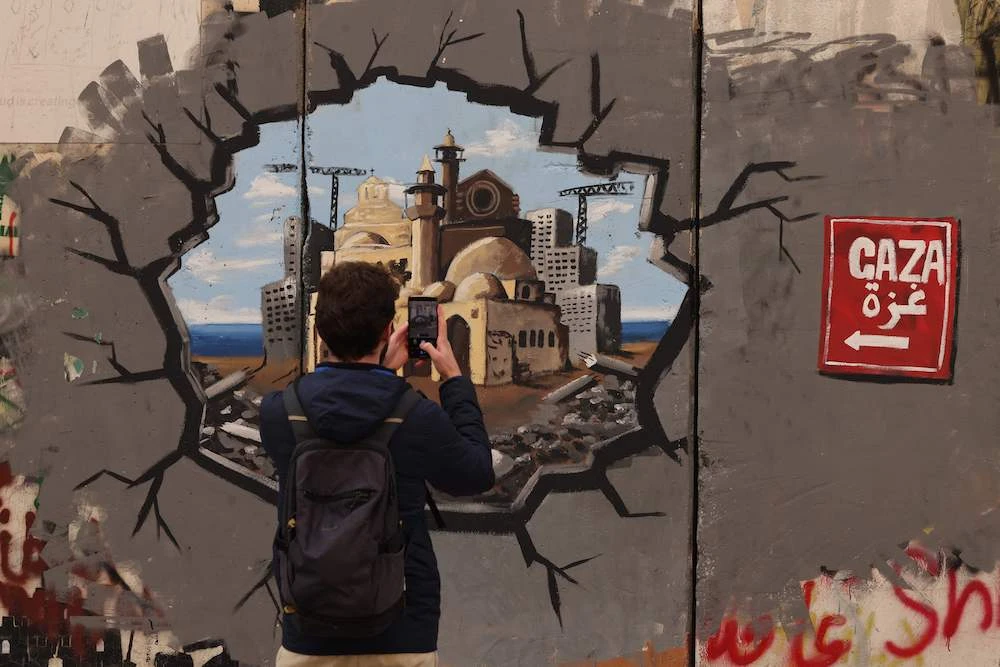 A man takes a picture of graffiti representing the reconstruction of Gaza in the occupied West Bank on Feb. 12, 2025. (AFP)