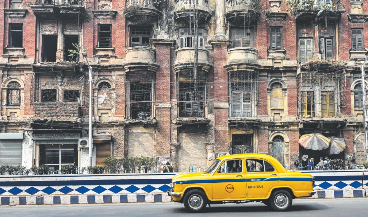 The driver of a Hindustan Ambassador yellow taxi rides past a heritage building in Kolkata. (AFP)