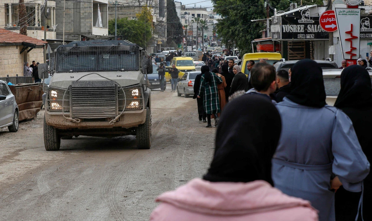 An Israeli army vehicle drives past people waiting to enter the Jenin camp for Palestinian refugees during an ongoing military operation, on February 19, 2025. (AFP)