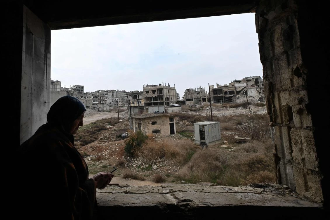 A displaced Syrian stands inside her dilapidated apartment, overlooking the destruction in Homs' Khaldiyeh neighborhood. (AFP)
