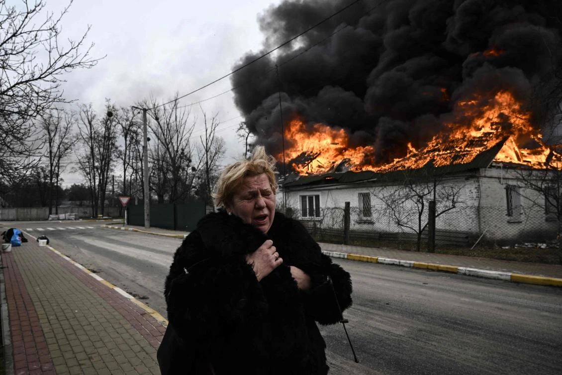 A woman stands in front of a house burning after being shelled in the city of Irpin, outside Kyiv. More than 1.2 million people have fled Ukraine into neighboring countries since Russia launched its full-scale invasion. (AFP)