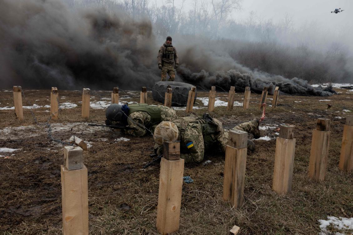 Ukrainian servicemen of the 24th Mechanized Brigade crawl under razor wire as black smoke billows nearby, during a training drill at an undisclosed location in the eastern region of Ukraine on Mar. 4, 2025, amid the Russian invasion of Ukraine. (AFP)