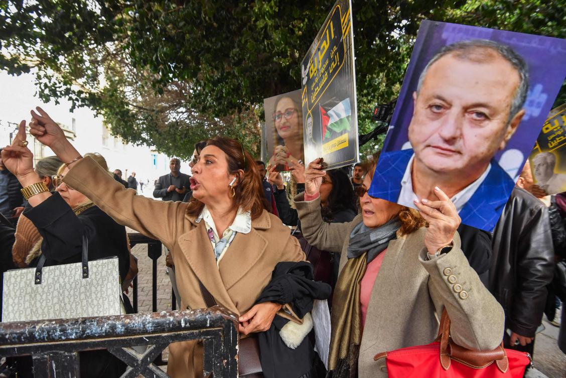 Dalila Ben Mbarek (L), lawyer and member of the defence committee of detainees accused of involvement in a conspiracy case against state security gestures alongside protesters lifting placards in front of the courthouse in Tunis on March 4, 2025. (AFP)