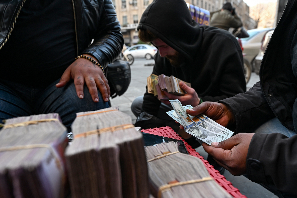 Currency traders exchange US dollars and Syrian liras on a street in Damascus. File/AFP