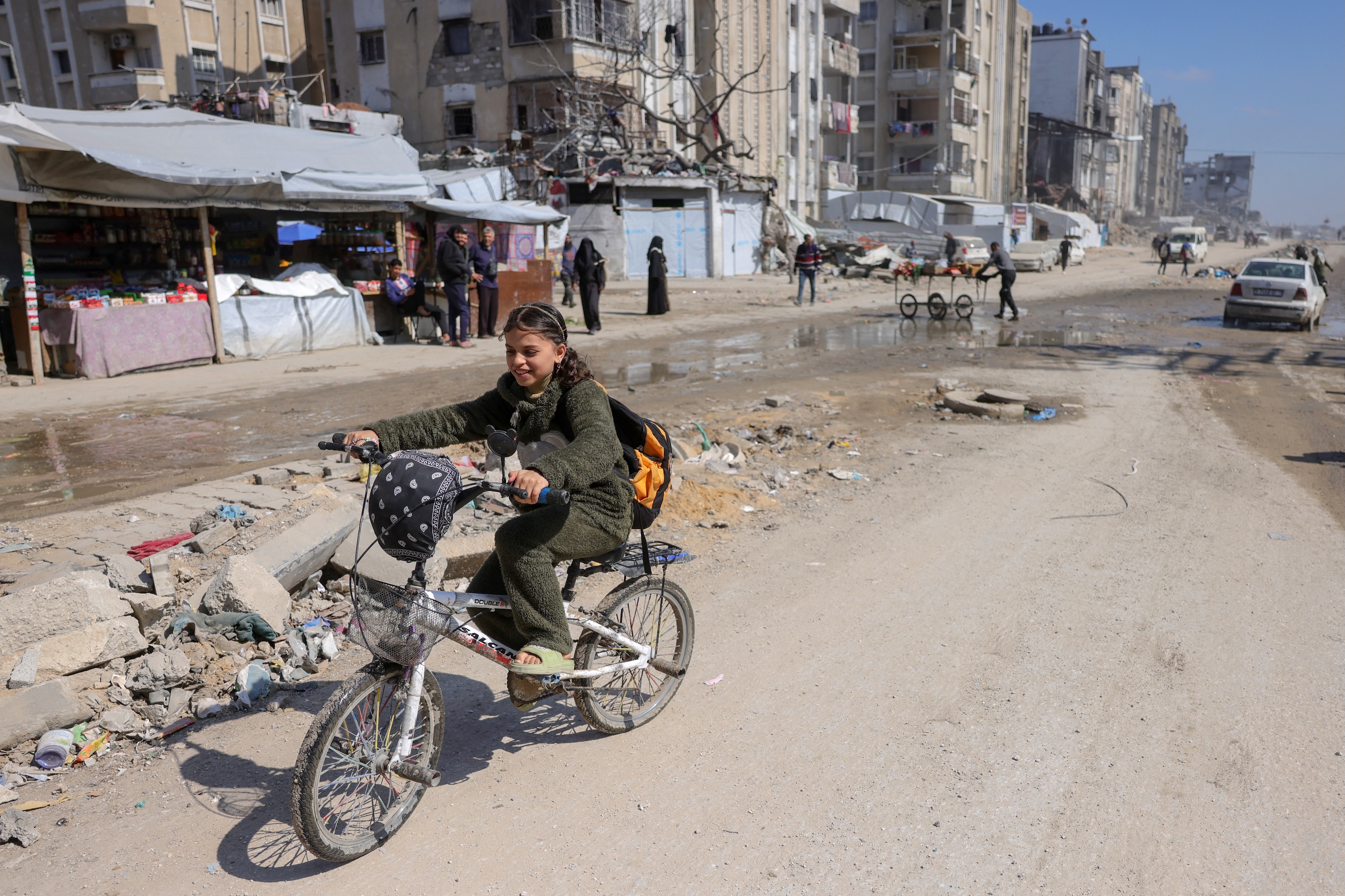 A Palestinian girl rides a bicycle past tents at a makeshift displacement camp west of Jabalia city in the northern Gaza Strip, March 11, 2025. (AFP)