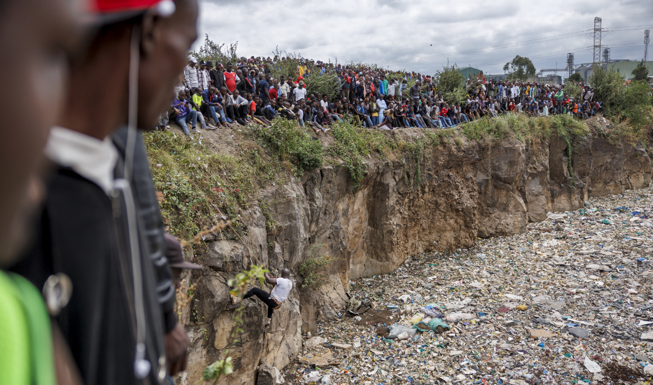 Crowds gather on the edge of an abandoned quarry to watch volunteers searching through a rubbish dump for human remains at Mukuru slum in Nairobi on July 14, 2024. (AFP)