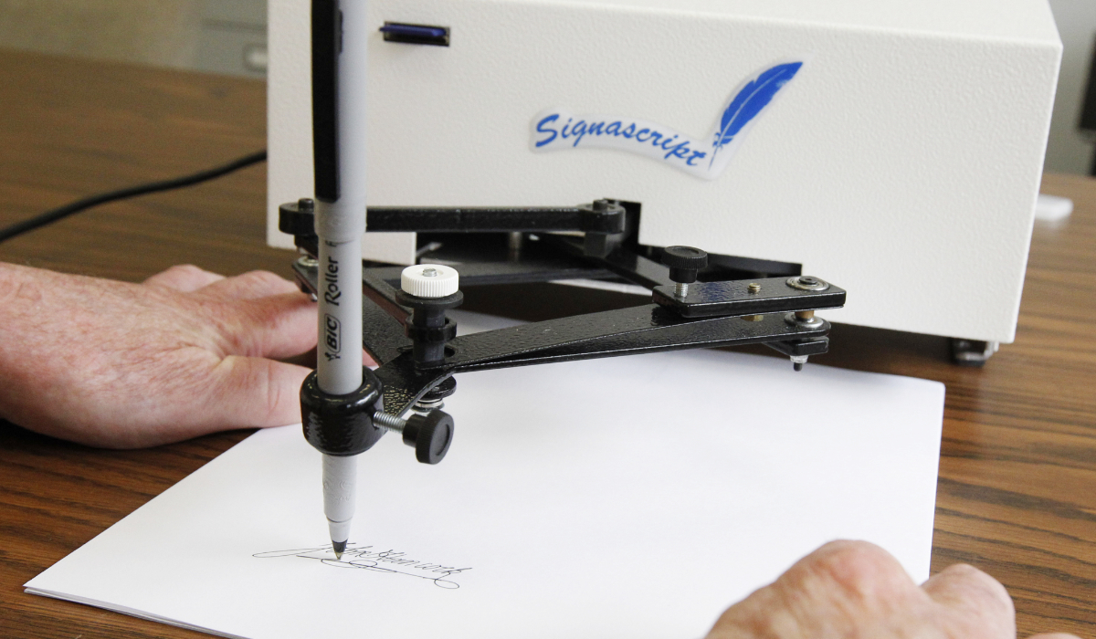 Damilic Corp. president Bob Olding anchors a sheet of paper as the Atlantic Plus, the Signascript tabletop model autopen, produces a signature at their Rockville, Md., office, June 13, 2011. (AP)