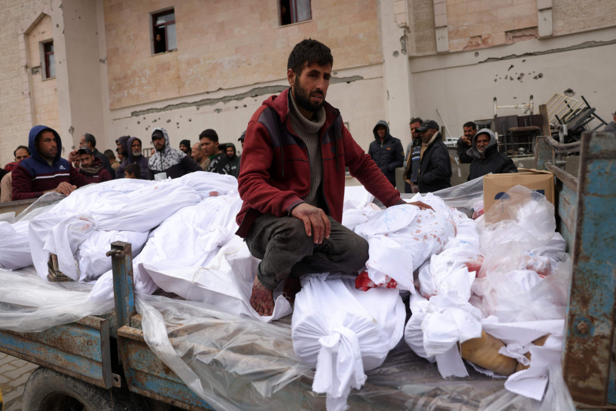 A Palestinian man sits atop bodies of victims killed in Israeli overnight airstrikes in the northern Gaza Strip on March 20, 2025. (AFP)