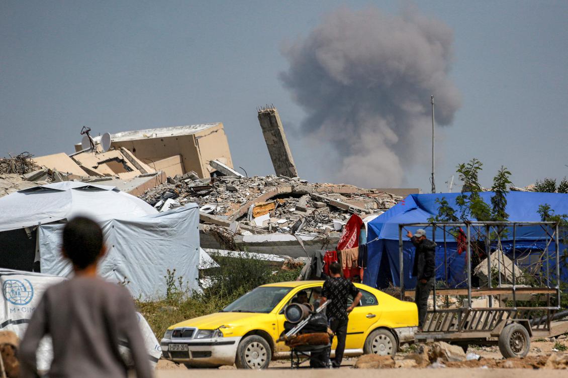 A boy looks on near a man talking to other men sitting in a vehicle while behind a cloud of smoke erupts from Israeli bombardment on the northern Gaza Strip, in Beit Lahia on March 25, 2025.(AFP)