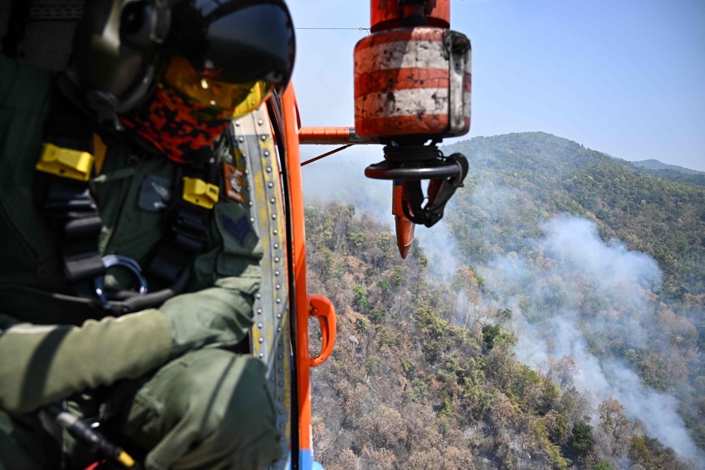 A Thai Department of Disaster Prevention and Mitigation personnel on a firefighting helicopter inspects fire spots to drop water to combat forest fires over Mae On district in the northern Thai province of Chiang Mai on March 26, 2025. (AFP)