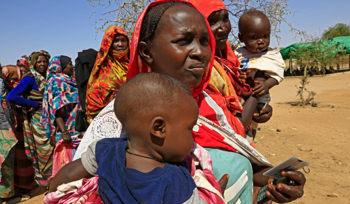 Displaced Sudanese women carry their children as they stand in queue as they wait for the arrival of the World Food Programme (WFP) trucks in the Otash internally displaced people's camp on the outskirts of Nyala town, the capital of South Darfur. (AFP file photo)
