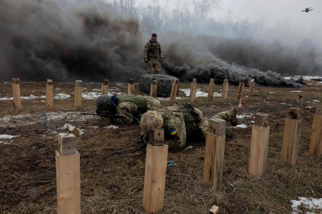 Ukrainian servicemen of the 24th Mechanized Brigade crawl under razor wire as black smoke billows nearby, during a training drill at an undisclosed location in the eastern region of Ukraine on Mar. 4, 2025, amid the Russian invasion of Ukraine. (AFP)
