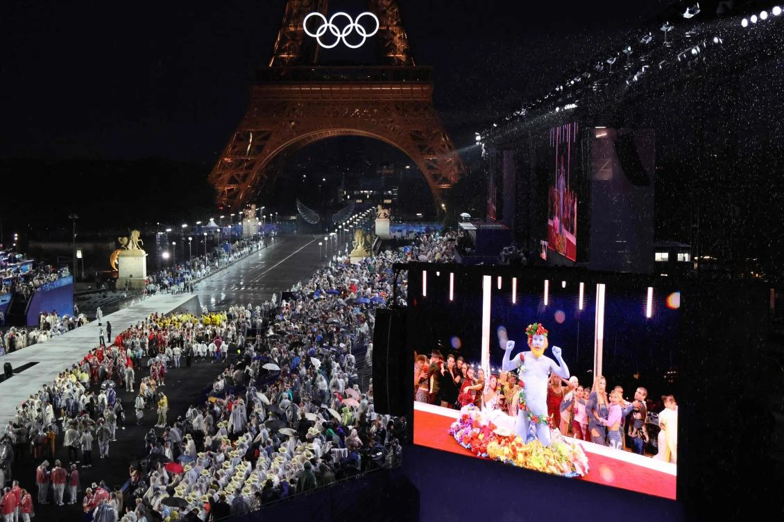 Delegations arrive at the Trocadero as spectators watch French singer Philippe Katerine performing on a giant screeen during the opening ceremony of the Paris 2024 Olympic Games in Paris on Jul. 26, 2024, as the Eiffel Tower is seen in the background. (AFP)