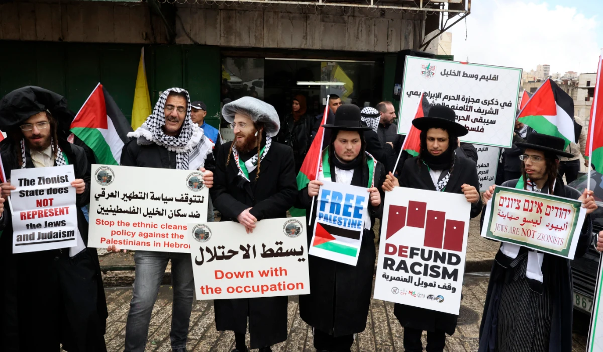 A Palestinian demonstrator stands among members of the Neturei Karta religious group of Haredi Jews, holding banners during a demonstration to commemorate the 1994 Ibrahimi Mosque massacre, in the centre of the West Bank town of Hebron, on February 25, 2022. (AFP)