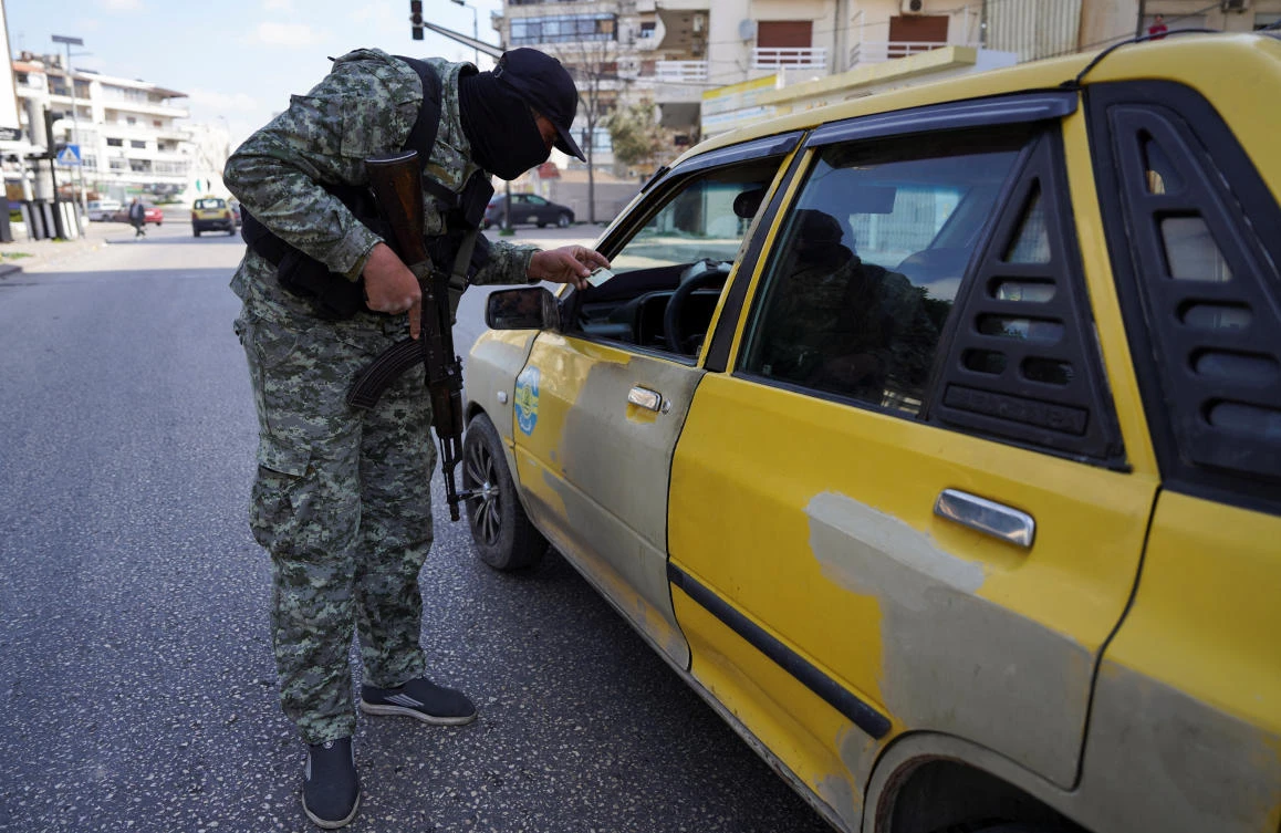A member of the Syrian security forces checks an ID of a person in Latakia on March 9, 2025. (Reuters)