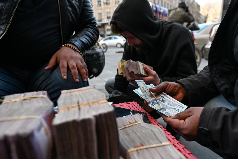 Currency traders exchange US dollars and Syrian liras on a street in Damascus. File/AFP