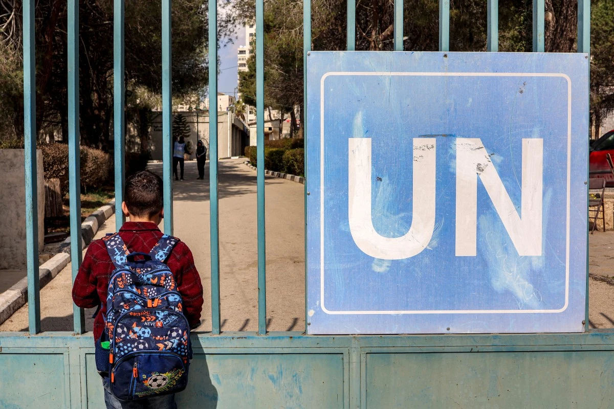 A boy stands outside the gate of the Kalandia vocational training centre (KTC), run by the United Nations Relief and Works Agency for Palestine Refugees (UNRWA), which was raided by Israeli forces earlier at the Qalandia camp for Palestinian refugees in the occupied West Bank on February 18, 2025. (AFP)