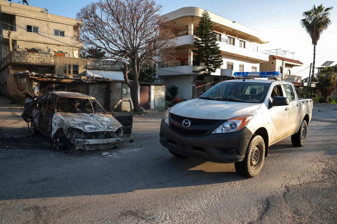 Security forces loyal to the interim Syrian government drive past a burned car at a checkpoint previously held by supporters of deposed president Bashar Assad, in the town of Hmeimim, in the coastal province of Latakia, on Mar. 11, 2025. (AFP)
