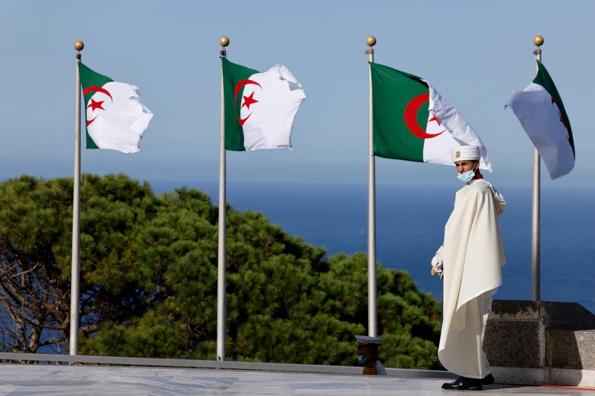 A man wearing a traditional cloth walks past national flags of Algeria near the Bay of Algiers in Algiers, Aug. 25, 2022. (AFP)