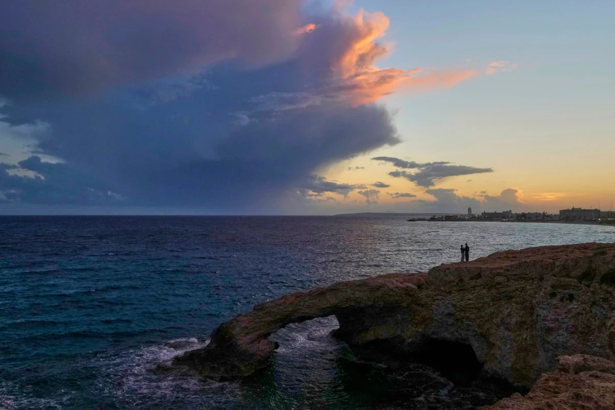 A couple stand on the rocks at the natural rock bridge that is named "Love Bridge", during sunset at Ayia Napa resort in the southeast Mediterranean island of Cyprus, on March 30, 2025. (AP Photo)