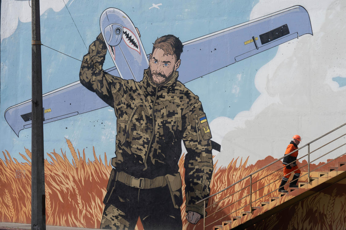 A municipal worker climbs stairs backdropped by a mural depicting a Ukrainian soldier carrying an Shark military drone, calling to donate for drones, in Kyiv, Apr. 3, 2025. (AP)