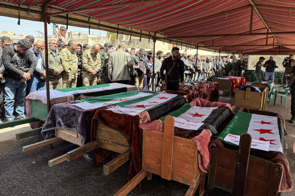 Mourners pray over the flag-draped coffins of people killed in reported Israeli shelling on Nawa in Syria's southern province of Daraa, during their funeral on April 3, 2025. (AFP)