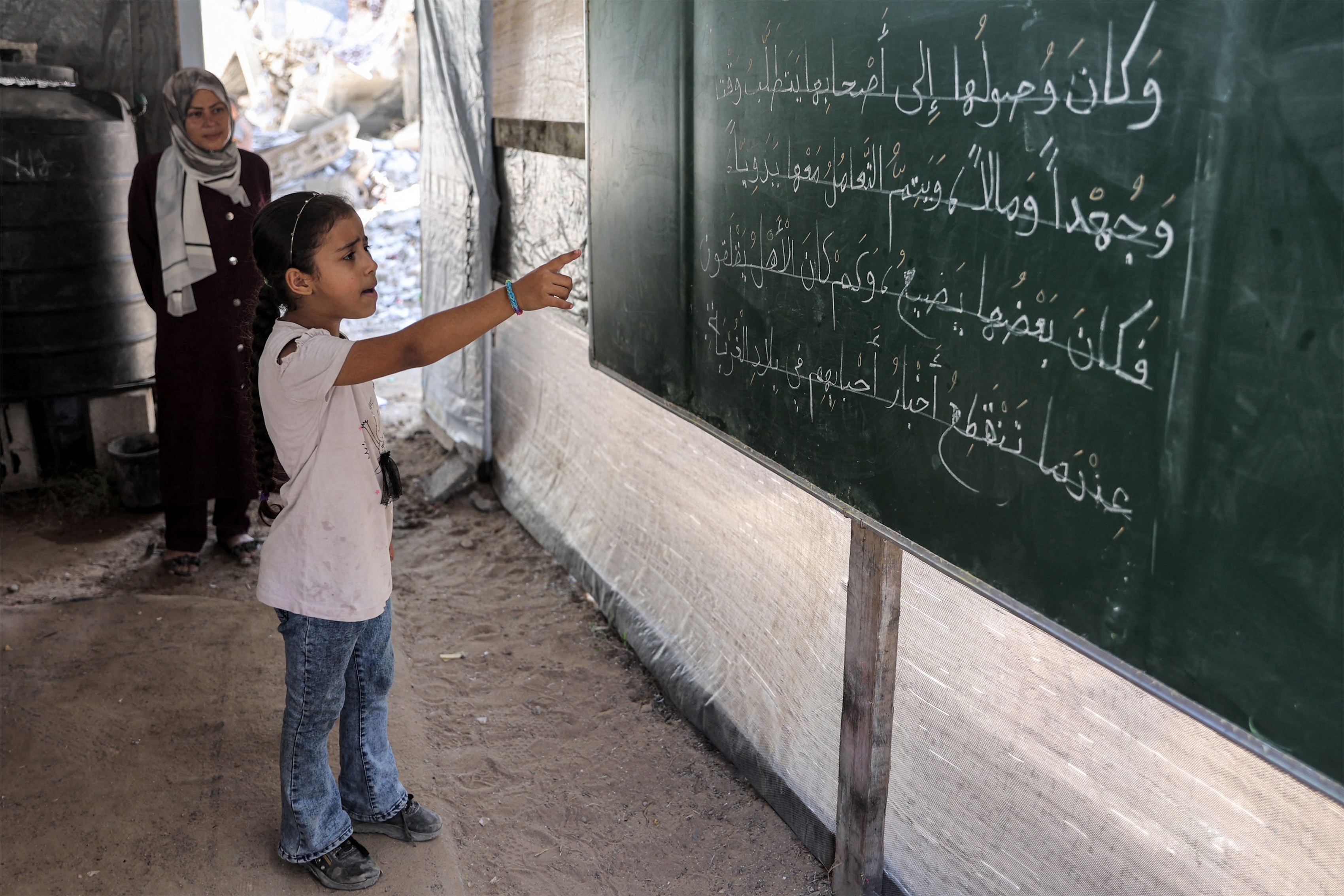 A girl stands before a blackboard during an Arabic grammar class in a tent being used as a make-shift educational centre for primary education students in Jabalia, northern Gaza Strip, Sep. 8, 2024. (AFP)