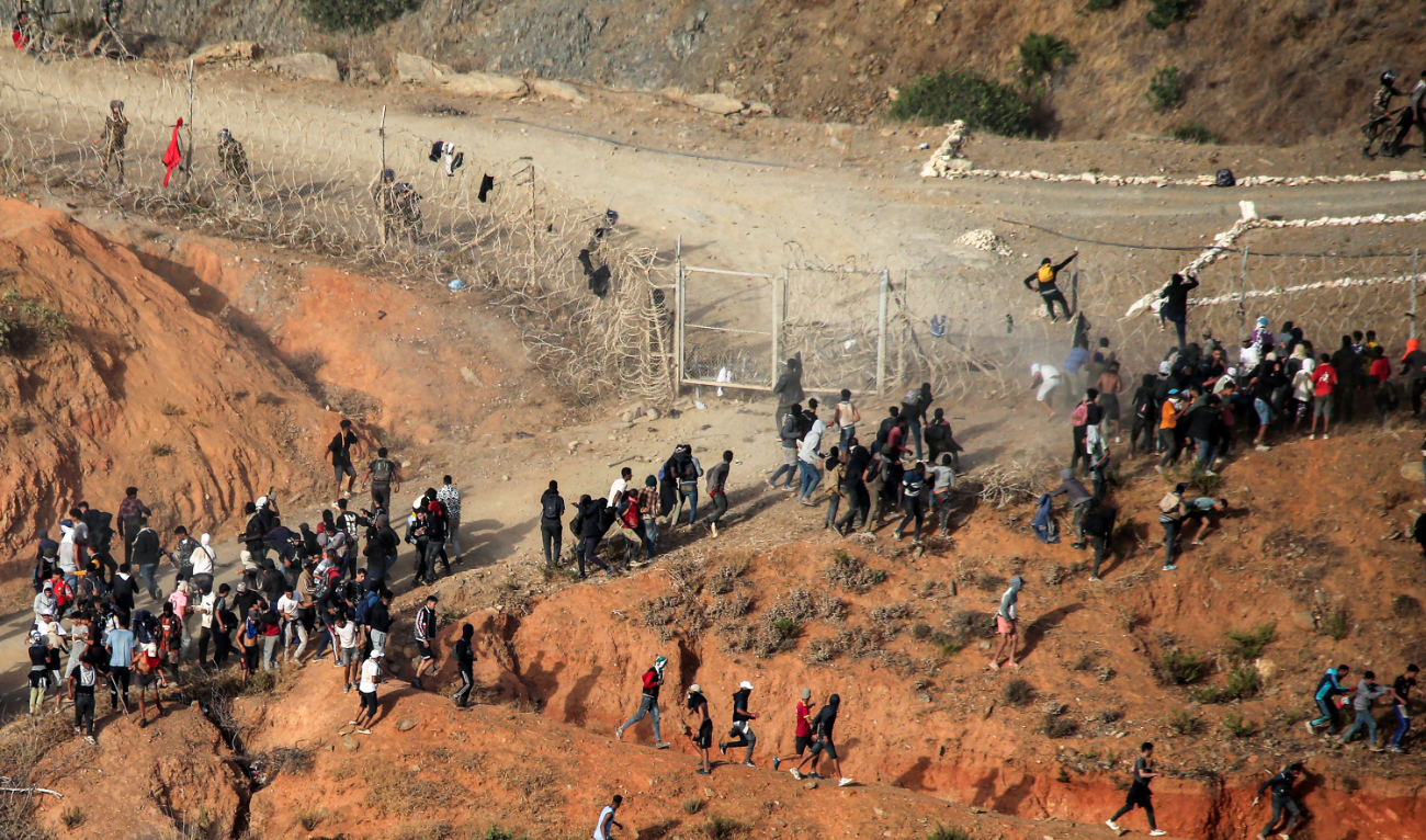 Migrants storm a barbed-wire fence as they attempt to cross the land border with Spain's African enclave of Ceuta near Fnideq in northern Morocco on September 15, 2024. (AFP/File)