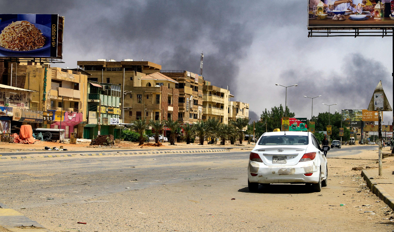 Smoke rises in the background as a car drives along an almost deserted street in Khartoum in this file photo taken on April 16, 2023. (AFP)