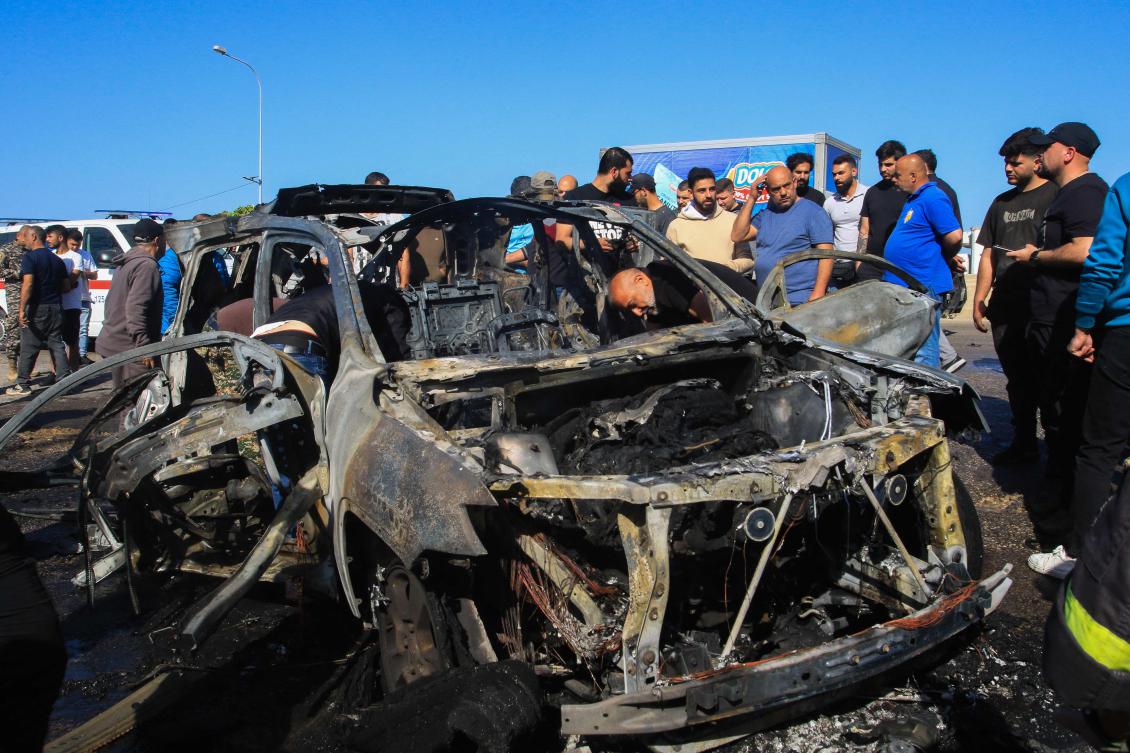 People inspect a burnt-out vehicle reportedly hit by an Israeli strike in Ghazieh, near Sidon, on April 18, 2025.(AFP)