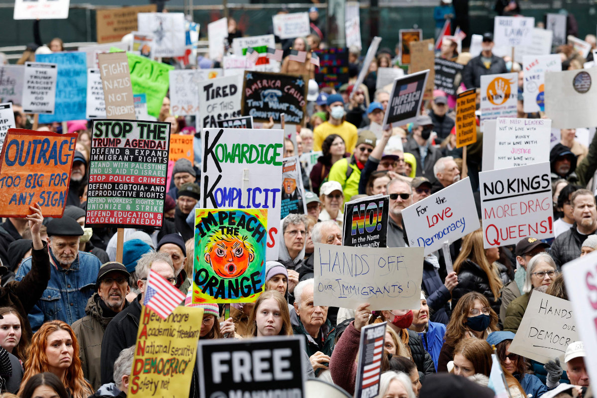 Demonstrators hold up signs during a rally in downtown Chicago, Illinois, on April 19, 2025 in protest against US President Donald Trump's policies and executive actions. (AFP)