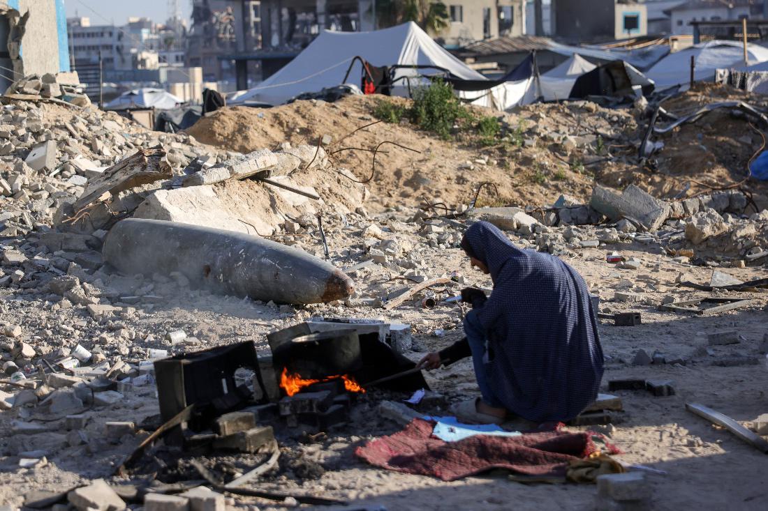 A displaced Palestinian woman cooks near an unexploded ordnance, with explosive materials removed and left behind by Israeli troops (AFP)