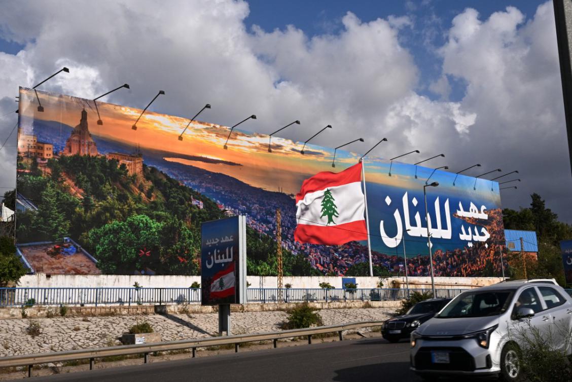 Commuters drive past a newly-installed billboard bearing the image of a Lebanese flag and a statement that reads in Arabic "Lebanon a new era". (File/AFP)
