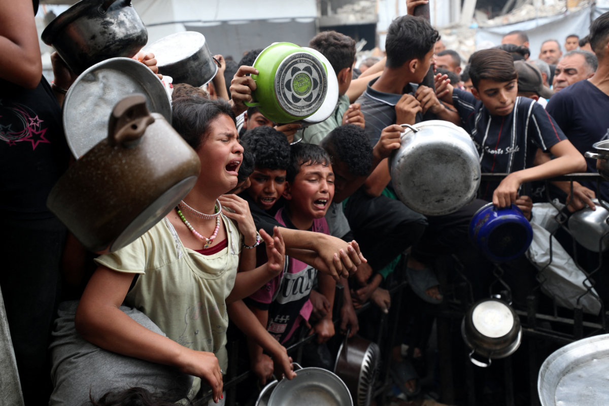 Children react as Palestinians wait to receive food cooked by a charity kitchen in Beit Lahia, northern Gaza Strip, on April 24, 2025. (REUTERS)
