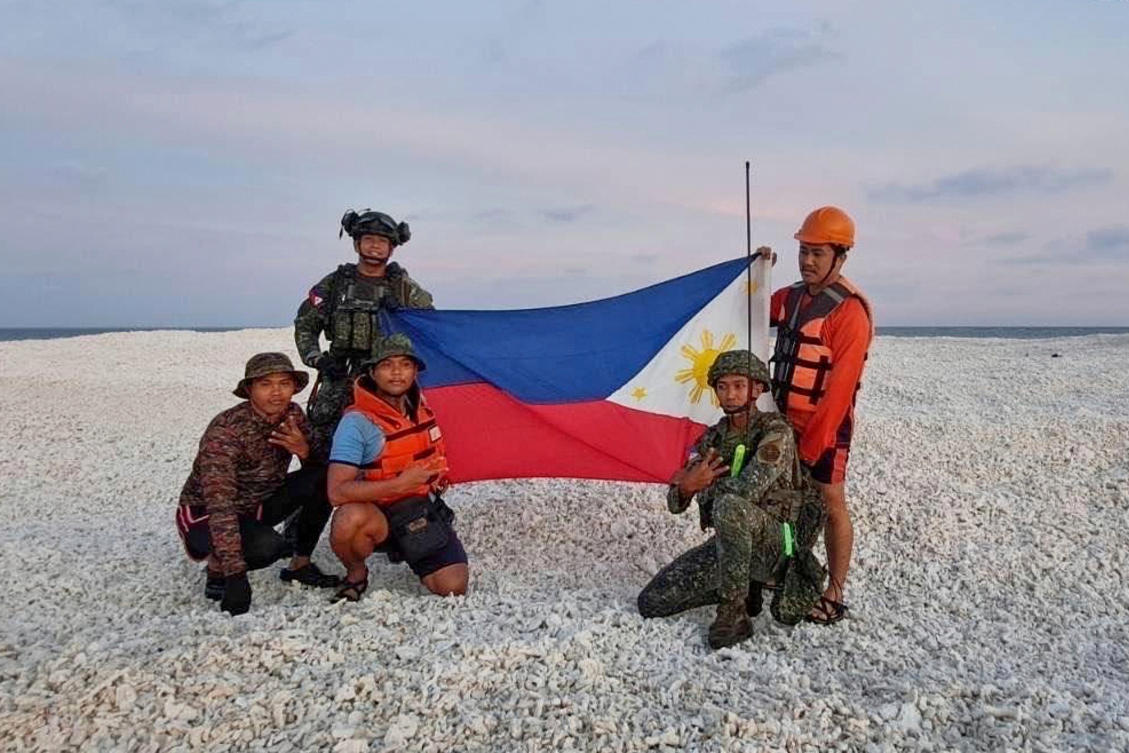 Philippine inter-agency members hold the Philippine flag as they visit Sandy Cay 2 at the South China Sea on April 27, 2025. (National Task Force West Philippine Sea via AP)