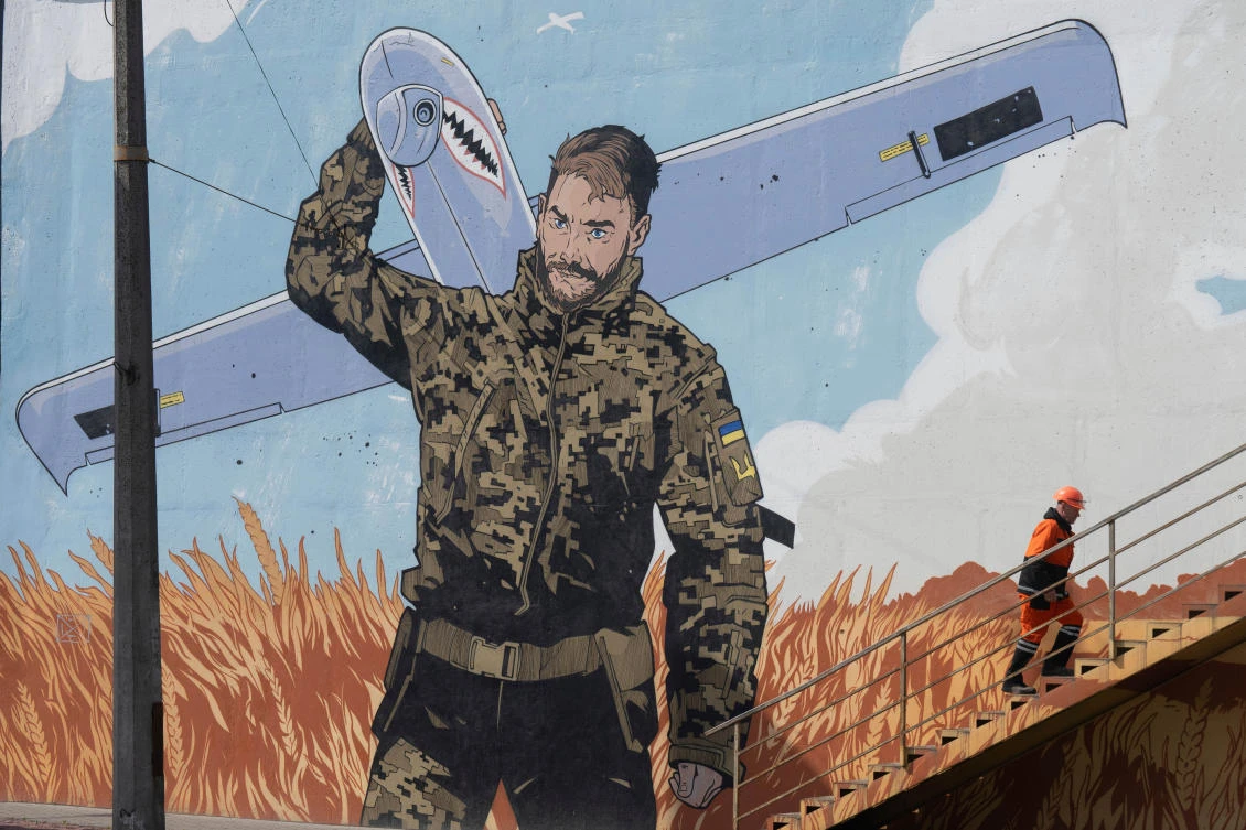 A municipal worker climbs stairs backdropped by a mural depicting a Ukrainian soldier carrying an Shark military drone, calling to donate for drones, in Kyiv, Apr. 3, 2025. (AP)