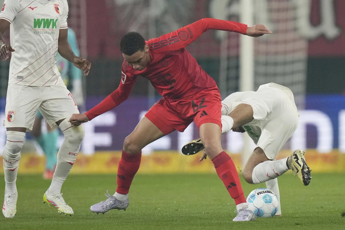 Augsburg’s Alexis Claude Maurice falls by Bayern’s Jamal Musiala during their Bundesliga match in Augsburg, Apr. 4, 2025. (AP)