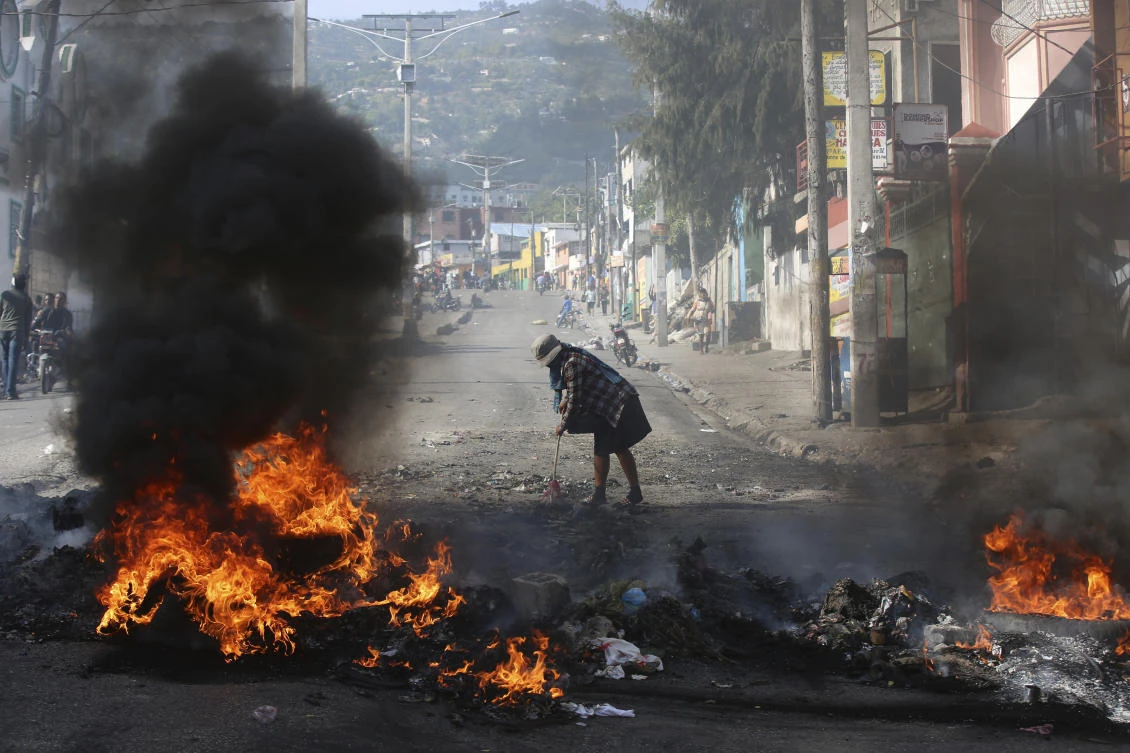 A woman sweeps debris next to a blazing barricade set up by demonstrators during a protest against insecurity in Port-au-Prince, Haiti on April 2, 2025. (AP)