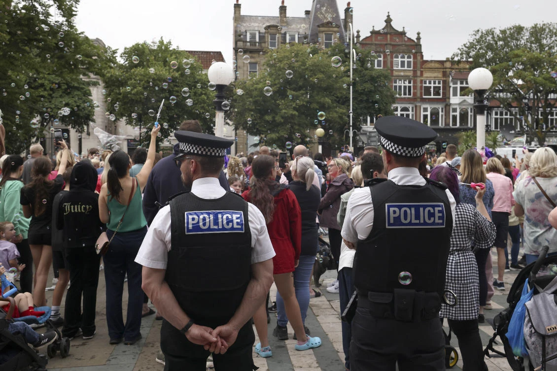 Police officers watch members of the public outside the Town Hall during a vigil to remember the victims of a stabbing attack in Southport, England. (File/AP)